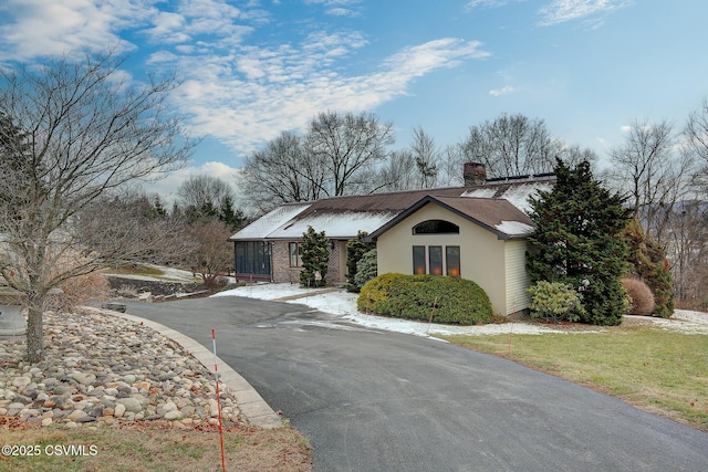 ranch-style house featuring driveway, a chimney, and a front yard