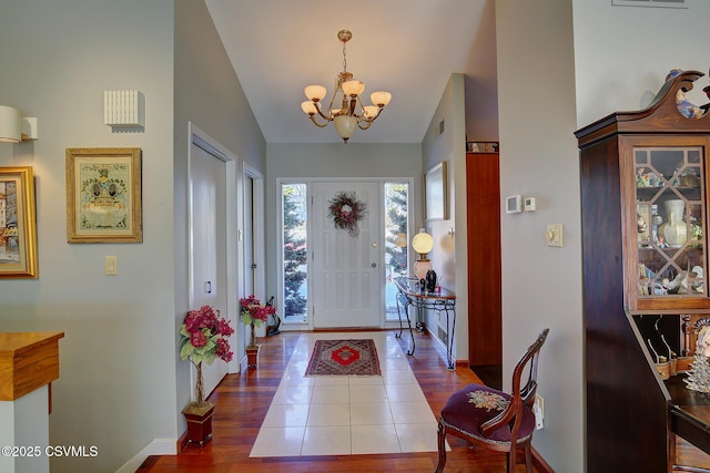 foyer featuring lofted ceiling, baseboards, a chandelier, and wood finished floors