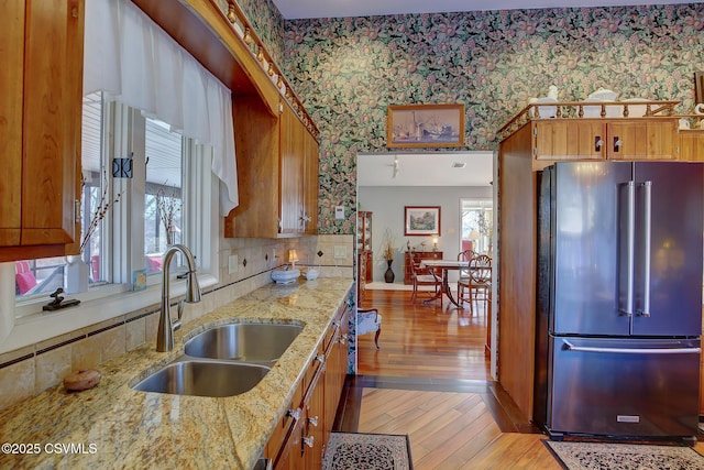 kitchen featuring brown cabinets, a sink, high end refrigerator, and wallpapered walls