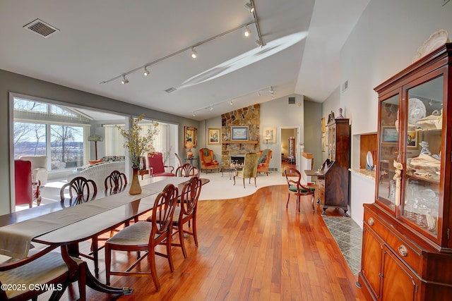 dining space featuring lofted ceiling, visible vents, a stone fireplace, and light wood finished floors