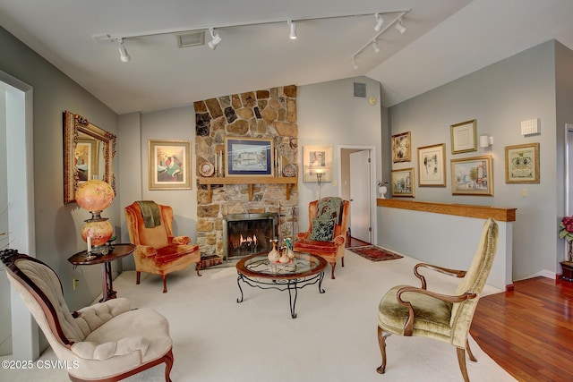 sitting room featuring lofted ceiling, visible vents, wood finished floors, and a stone fireplace