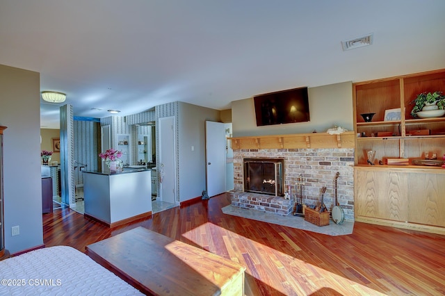 living area with a brick fireplace, wood finished floors, visible vents, and baseboards