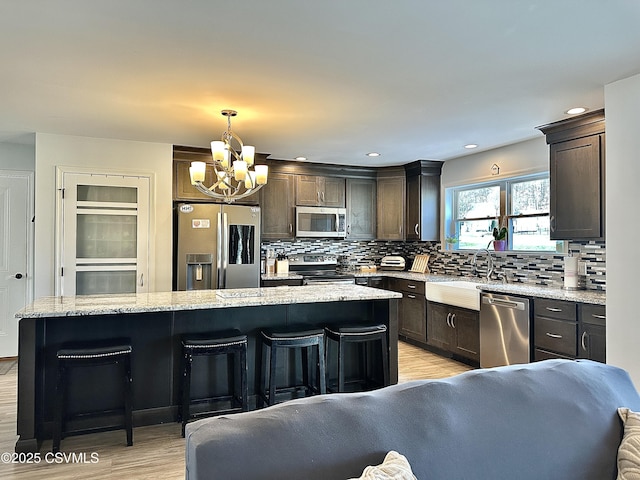 kitchen featuring a breakfast bar, light hardwood / wood-style flooring, appliances with stainless steel finishes, decorative light fixtures, and a kitchen island