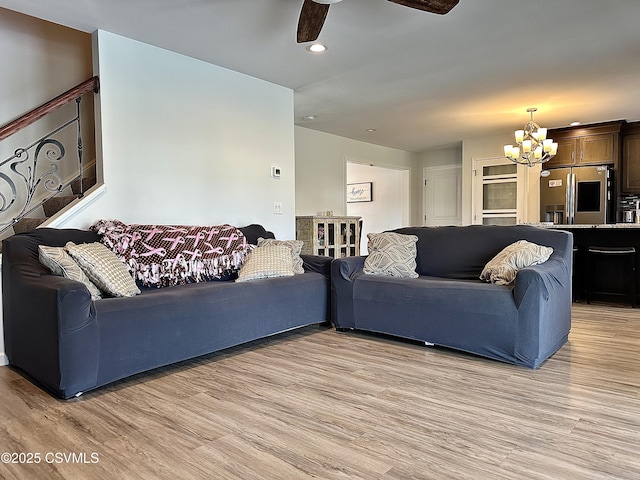 living room with ceiling fan with notable chandelier and light hardwood / wood-style floors