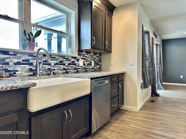 kitchen with tasteful backsplash, stainless steel dishwasher, dark brown cabinets, sink, and light hardwood / wood-style flooring