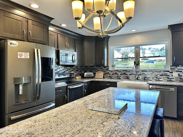 kitchen with light stone countertops, appliances with stainless steel finishes, sink, pendant lighting, and an inviting chandelier