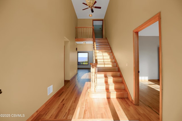 stairs featuring ceiling fan, a towering ceiling, and hardwood / wood-style floors