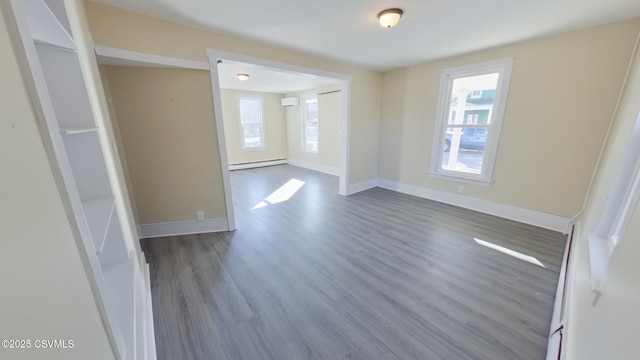 empty room featuring baseboard heating, wood-type flooring, a wall mounted AC, and a healthy amount of sunlight