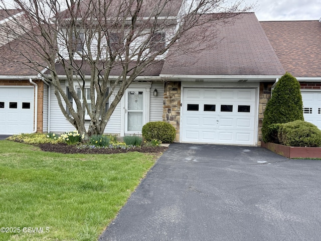 view of front facade featuring roof with shingles, a front yard, driveway, and stone siding
