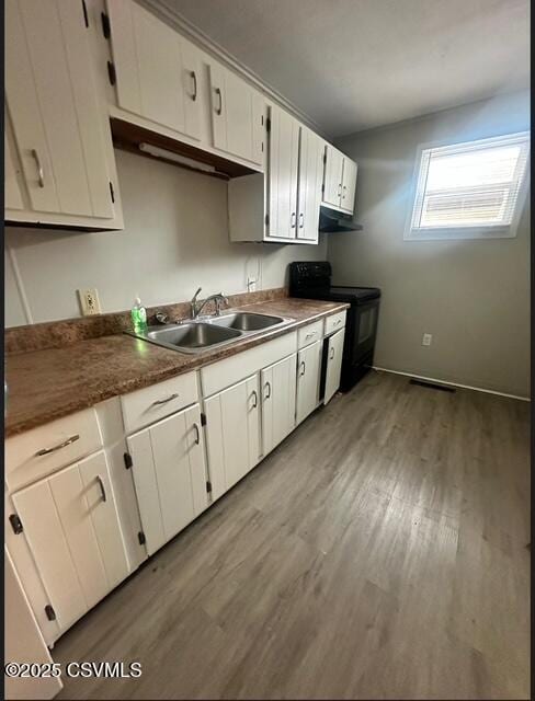 kitchen with black / electric stove, sink, white cabinetry, and light hardwood / wood-style floors