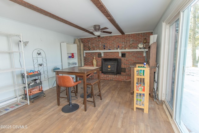 dining room with a wood stove, beam ceiling, hardwood / wood-style flooring, and ceiling fan