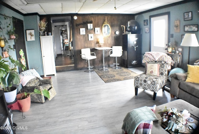 living room with hardwood / wood-style flooring, indoor bar, ornamental molding, and wood walls