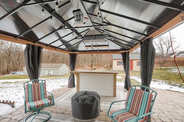 snow covered patio with area for grilling, a gazebo, and an outdoor structure