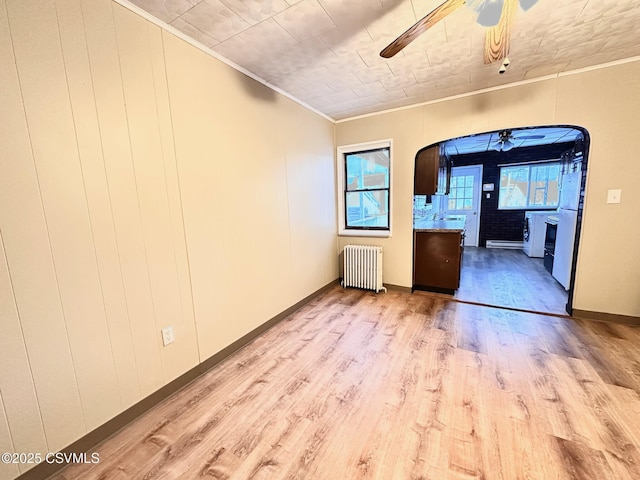 empty room with ceiling fan, sink, crown molding, radiator, and light wood-type flooring