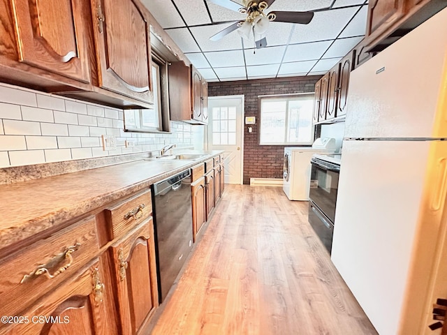 kitchen featuring white fridge, black dishwasher, light wood-type flooring, a drop ceiling, and sink