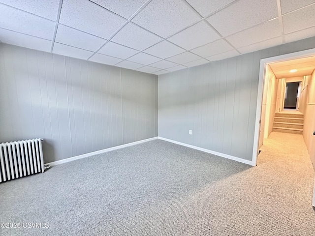 unfurnished room with carpet, radiator heating unit, and a drop ceiling