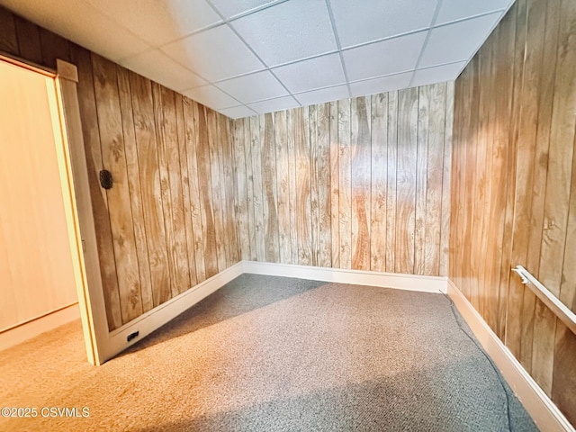 spare room featuring carpet, a drop ceiling, and wood walls