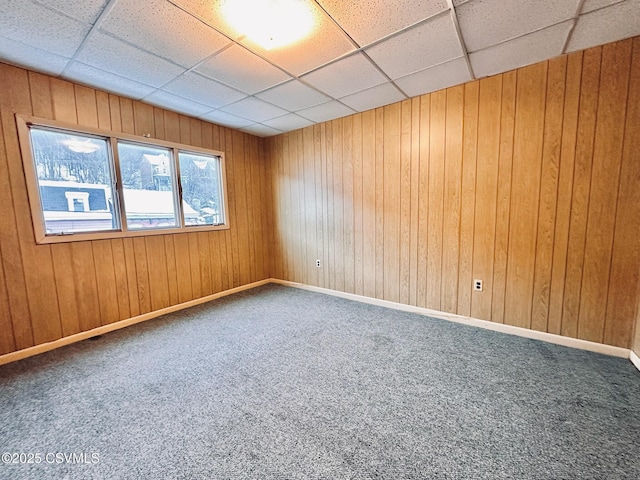 carpeted empty room featuring a drop ceiling and wooden walls