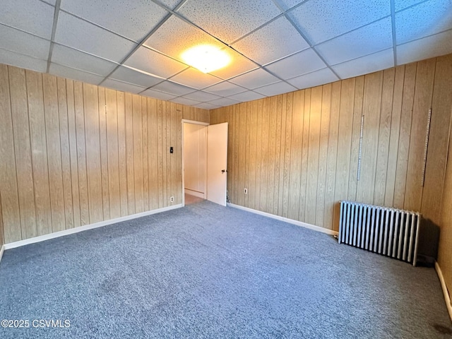 empty room with radiator, a paneled ceiling, carpet floors, and wood walls