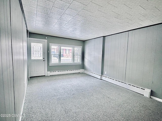 spare room featuring light colored carpet, baseboard heating, and wooden walls