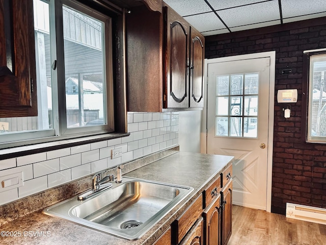 kitchen with light wood-type flooring, a drop ceiling, sink, and brick wall