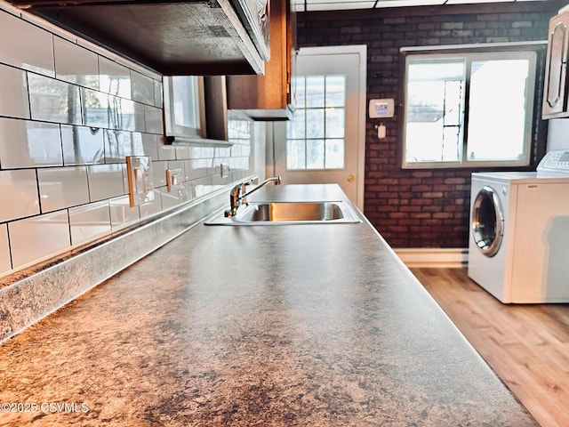 kitchen featuring light hardwood / wood-style floors, sink, brick wall, and washer / dryer