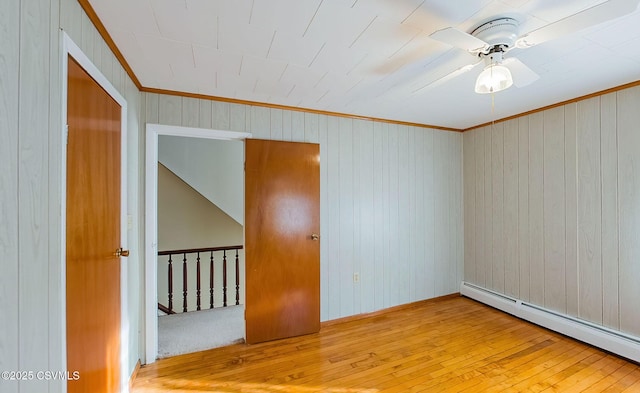 spare room featuring crown molding, wood-type flooring, ceiling fan, and baseboard heating