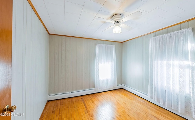 unfurnished room featuring baseboard heating, ceiling fan, ornamental molding, and hardwood / wood-style floors