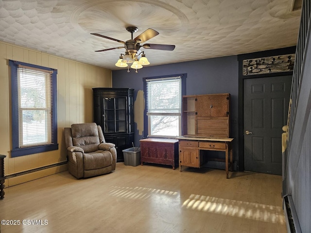 sitting room featuring light wood-type flooring, ceiling fan, a textured ceiling, and a baseboard heating unit