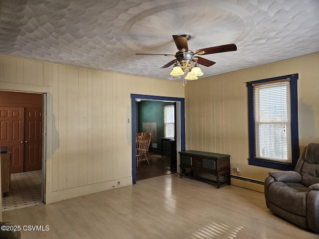 living room featuring ceiling fan, wood walls, light hardwood / wood-style floors, a textured ceiling, and a baseboard radiator