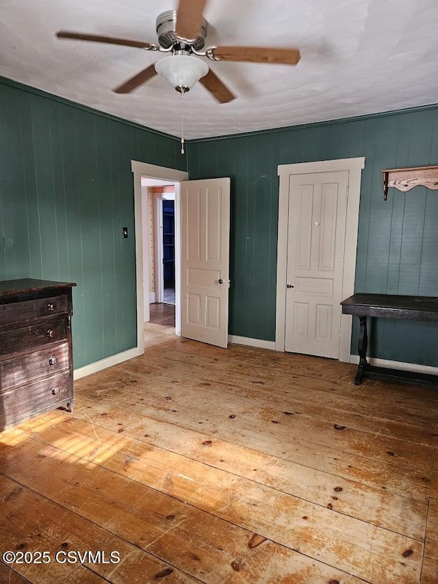 unfurnished bedroom featuring ceiling fan, wood walls, and hardwood / wood-style floors