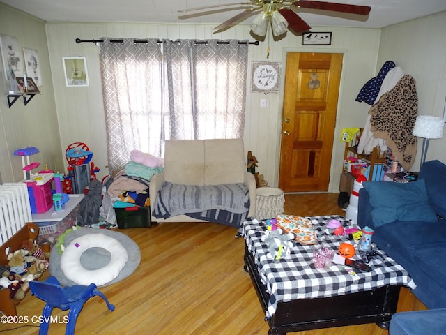 living room featuring radiator, hardwood / wood-style flooring, wooden walls, and ceiling fan