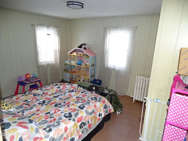 bedroom with multiple windows, radiator, hardwood / wood-style floors, and wood walls