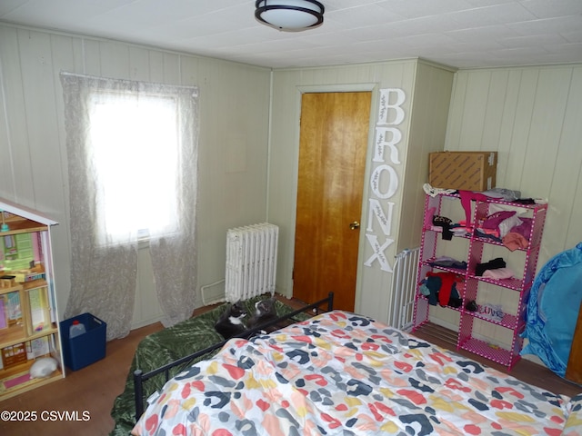 carpeted bedroom with radiator heating unit, multiple windows, and wood walls