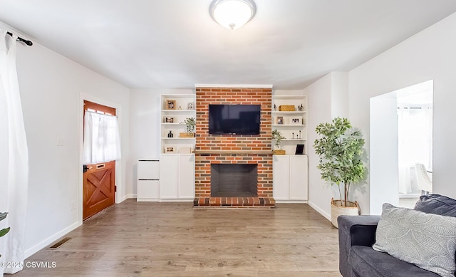 living room with light wood-type flooring, a fireplace, and built in shelves