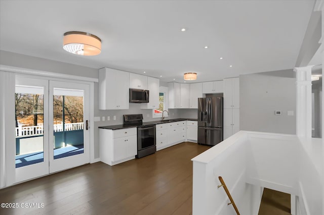 kitchen with sink, dark wood-type flooring, stainless steel appliances, decorative columns, and white cabinets