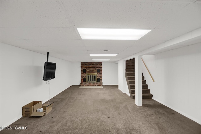 basement featuring a brick fireplace, a drop ceiling, and carpet