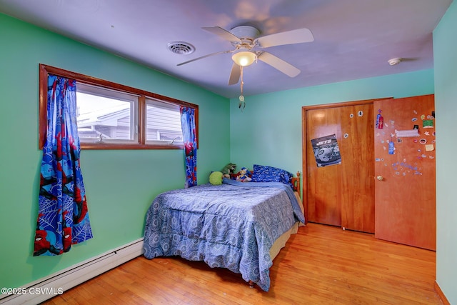 bedroom with a baseboard heating unit, ceiling fan, and light hardwood / wood-style flooring