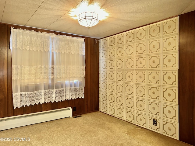 spare room featuring light colored carpet, baseboard heating, and wood walls