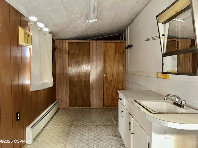 kitchen with baseboard heating, wooden walls, sink, and white cabinets