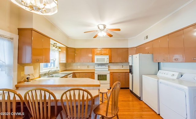 kitchen featuring washer and dryer, sink, white appliances, kitchen peninsula, and light wood-type flooring