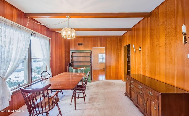 dining area with beamed ceiling, wooden walls, light carpet, and a chandelier