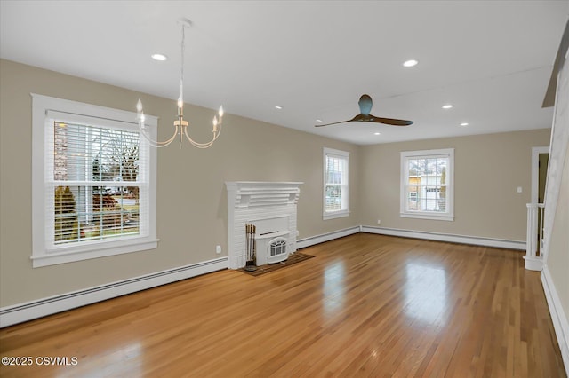 unfurnished living room featuring ceiling fan with notable chandelier, baseboard heating, and light hardwood / wood-style flooring