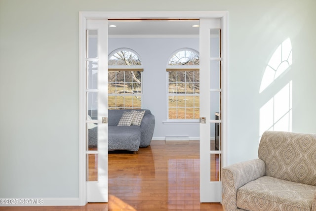 interior space featuring wood-type flooring, a baseboard heating unit, crown molding, and french doors