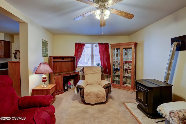 living area featuring ceiling fan, light colored carpet, and a wood stove