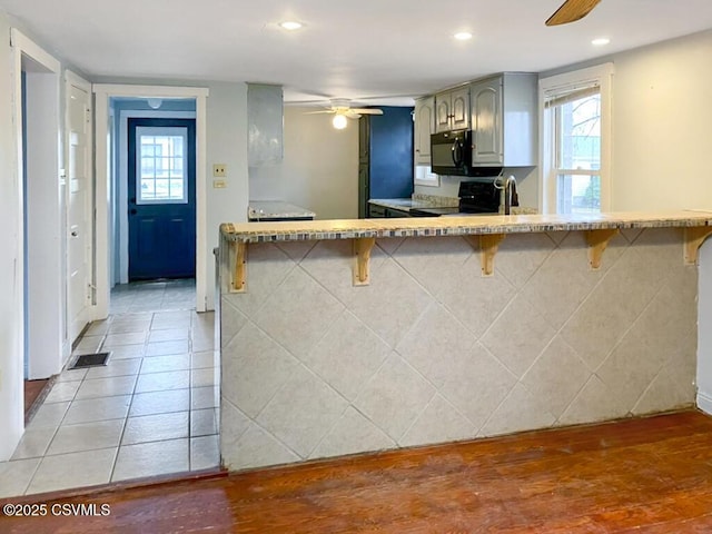 kitchen featuring gray cabinetry, ceiling fan, a kitchen breakfast bar, and electric stove