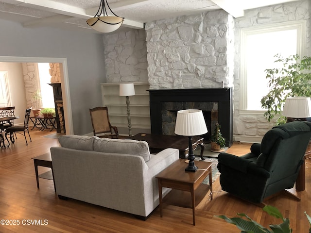 living room featuring hardwood / wood-style flooring, a fireplace, a textured ceiling, and beamed ceiling