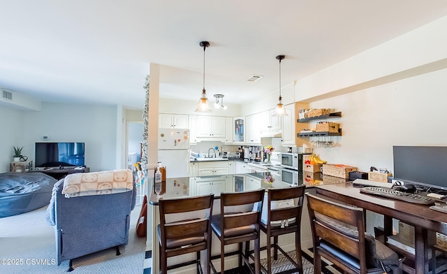 kitchen with a breakfast bar area, hanging light fixtures, kitchen peninsula, white fridge, and white cabinets