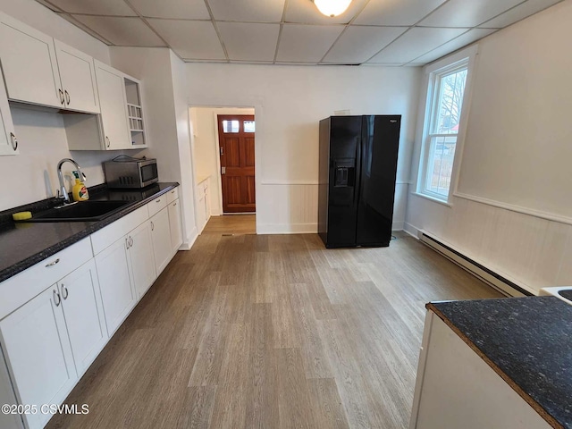 kitchen with stainless steel microwave, a baseboard heating unit, black refrigerator with ice dispenser, a paneled ceiling, and a sink