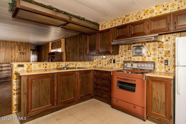 kitchen featuring ventilation hood, sink, white fridge, range, and kitchen peninsula